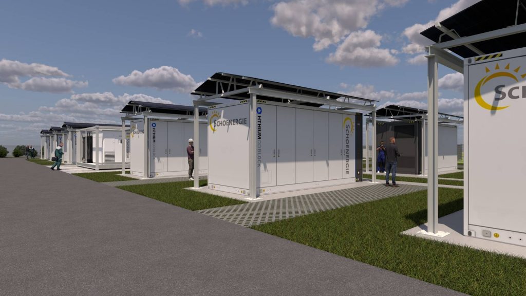 Nahaufnahme mehrerer weisser Container-Einheiten auf gepflastertem Untergrund innerhalb der Anlage, mit Personen in Arbeitskleidung, die an den Containern arbeiten. Auf den Containern ist das Logo „Schoenergie“ sichtbar. Die Container sind mit Solarpanels ausgestattet und Teil eines Forschungsprojekts zur Netzstabilität.